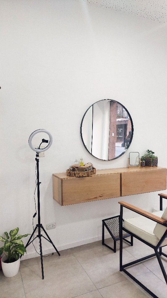 El espacio de Nala Beauty: sillón, mueble de madera, espejo redondo, aro de luz y una planta
